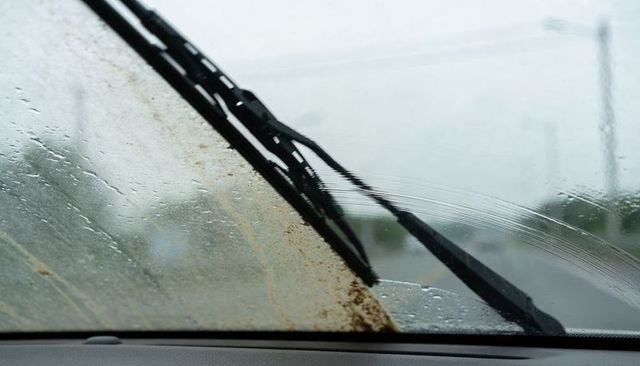 Windshield wipers clearing mud-smeared glass on rainy road, restoring driving visibility