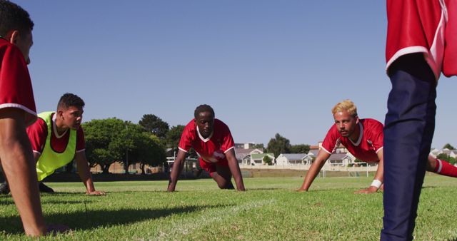 Soccer players engage in push-up exercises on a grassy field during an outdoor practice session. Ideal for materials related to sports training, fitness programs, teamwork, athletic drills, and outdoor activities.