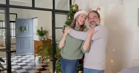 Senior couple embracing by christmas tree with holiday accessories