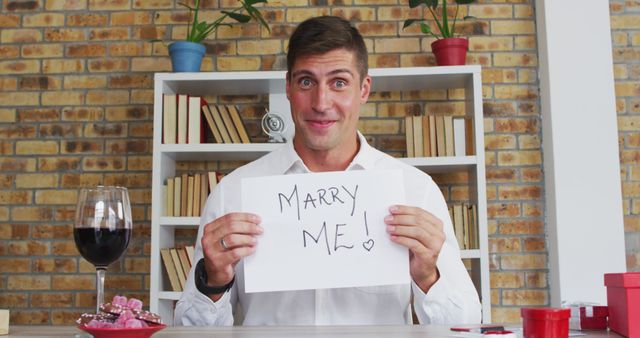 Caucasian man making image call holding handwritten sign making marriage proposal and celebrating acceptance. online communication during quarantine lockdown.