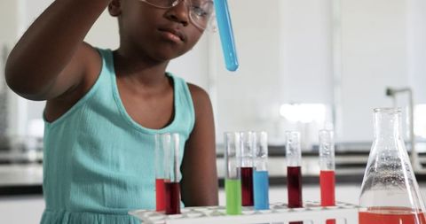 Young african american girl conducting colorful chemistry experiment in school laboratory