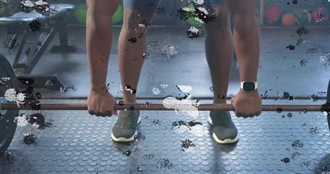 Gripping athlete lifting Olympic barbell deadlift on rubber dimple floor with smartwatch
