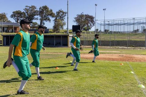 Baseball team warming up stretching and sprinting on grass field with cones and dugout