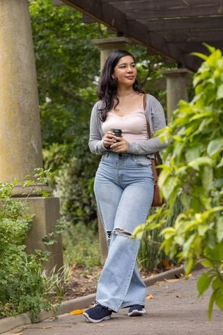 African american woman standing under pergola holding coffee cup in park wearing denim jeans