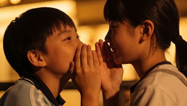 Whispering classmates sharing secret in warm dusk school hallway close-up intimate moment