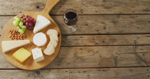 Image of cheeses, bread, grapes and nuts on board and red wine on wooden table, with copy space. quality light food snack and drink.