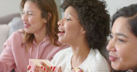 Friends Enjoying Cozy Movie Night on Sofa Sharing Popcorn, Laughing and Chatting Together