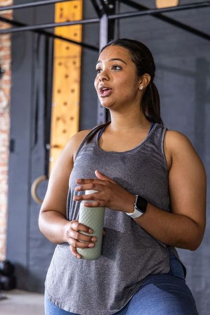 Female athlete pausing between sets holding textured bottle exhaling during gym workout