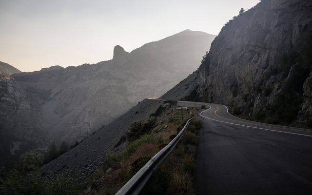 Image shows a winding mountain road at sunset in a remote area, perfect for using in travel blogs, outdoor adventure promotions, and nature-themed advertisements. The image highlights the rugged beauty of nature and the allure of exploring less-traveled paths.