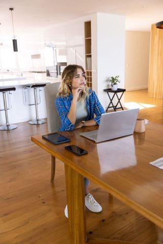 Thoughtful Young Woman Working on Laptop in Modern Kitchen