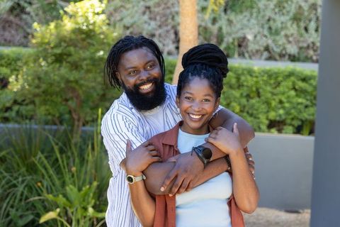 Smiling african american couple embracing in sunlit garden courtyard, casual love portrait