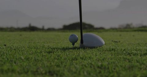 Closeup golf driver aligning with ball on tee on lush fairway ready for powerful tee shot