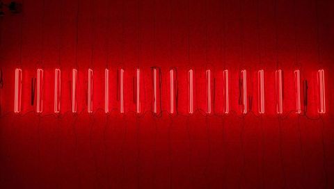 Glowing vertical red neon tube installation spanning gallery wall with visible cables