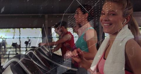 Smiling woman running on treadmill with towel and earbuds in bright gym group cardio scene