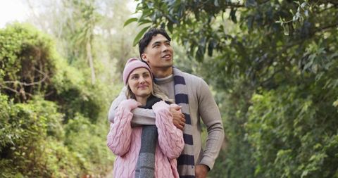 Multiracial couple embracing on woodland path wearing cozy knit scarves and winter layers
