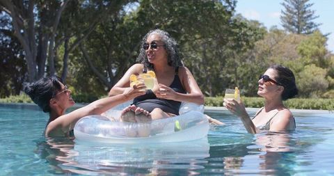 Women relaxing on clear inflatable tube in pool toasting citrus cocktails