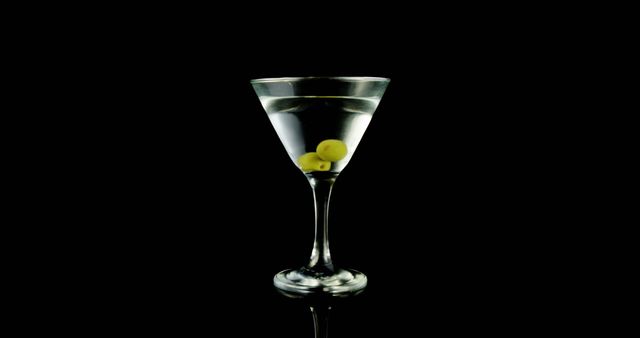 A classic martini with olives is presented in an elegant glass against a black background, with copy space. Its simplicity and contrast convey a sense of sophistication and timeless appeal in cocktail culture.