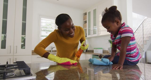 African american mother and daughter cleaning countertops and laughing in kitchen. staying at home in self isolation during quarantine lockdown.