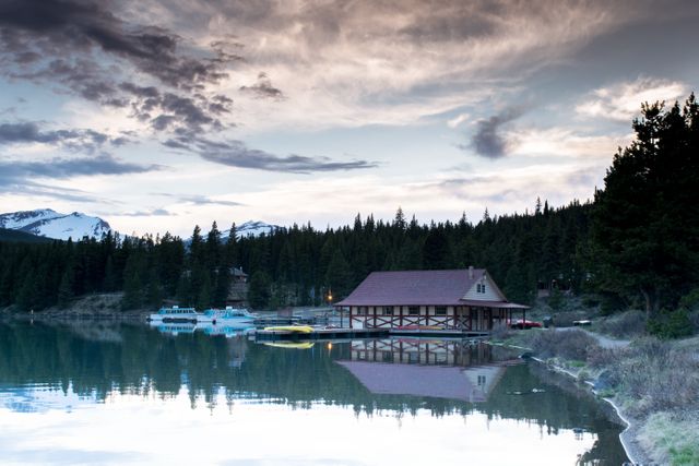 Docked along a calm lake, the wooden house mirrors in the still waters under a dramatic twilight sky. This image perfectly captures tranquility and the beauty of nature, making it ideal for promoting retreat getaways, outdoor activities, and travel destinations. Use in advertisements, websites, or brochures focused on vacation rentals, outdoor lifestyles, or nature retreats.