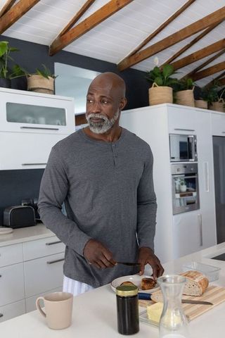 Senior african american man preparing breakfast in modern minimalist kitchen, slicing bread