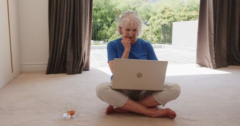 Senior woman laptops by bright window in serene home setting