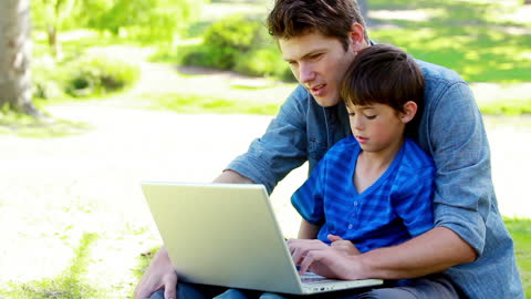 Father and Son Bonding Over Laptop in Relaxing Park