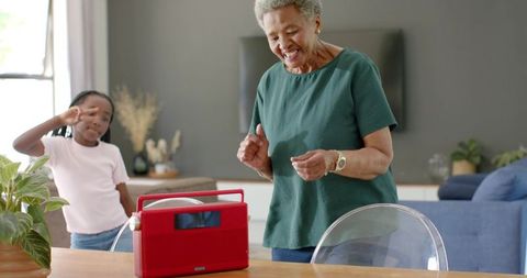 Senior african grandmother dancing with granddaughter beside red radio, joyful home moment