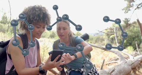 Female hikers studying smartphone with molecular ar overlays while exploring nature trail