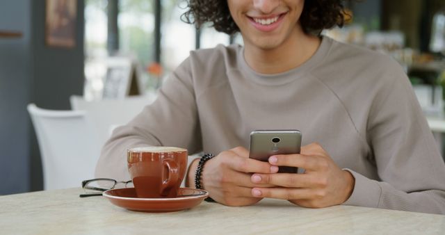 Smiling Young Man Enjoying Coffee and Using Smartphone in Cafe - Download Free Stock Images Pikwizard.com