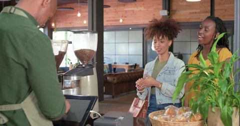 Women using tablet pos to order coffee at cozy cafe counter