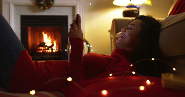 Woman enjoying time by the fireplace while using a smartphone. This can be used for promoting holiday traditions, winter relaxation, and technology in everyday home settings. Perfect for lifestyle blogs, social media posts, or advertising home coziness and technology.