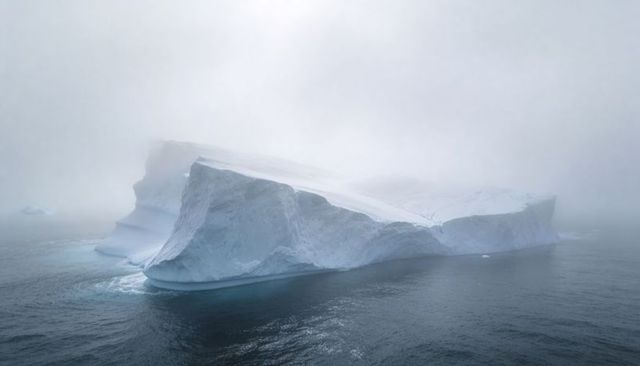 Tabular iceberg drifting through foggy polar sea, moody minimalist arctic landscape