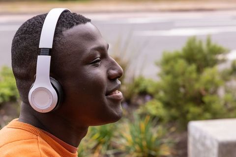 African american man wearing headphones smiling outdoors near urban greenspace casual portrait