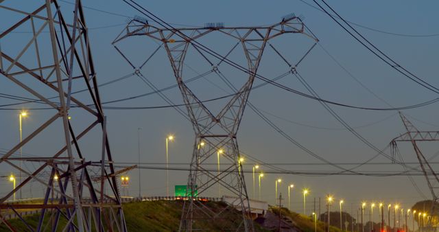 High voltage power lines are intersecting against a clear night sky, accompanied by illuminated street lights below. This photo is perfect for illustrating urban infrastructure, electrical grids, and power transmission themes for energy publications, city planning visuals, and industrial presentations.