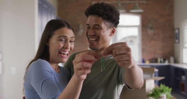 Joyful young couple celebrating moving into their new home, holding keys and smiling. Ideal for articles or advertisements related to real estate, home buying, moving services, and new homeownership.