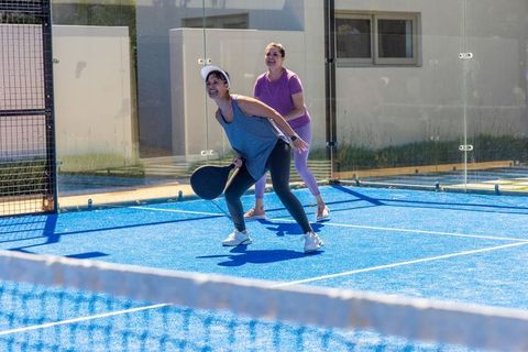 Hispanic and african american women playing padel on vibrant blue court, doubles action