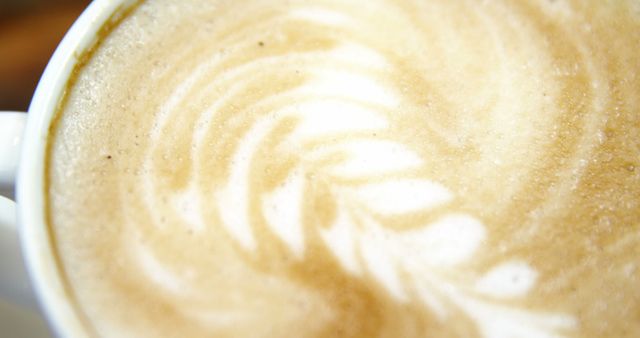This image shows a close-up of a creamy latte with elegant swirl art on top. Perfect for use in promotional materials for coffee shops, blogs about coffee culture, or social media posts about morning routines and relaxation. It highlights the skill of baristas and the beauty of well-crafted drinks.