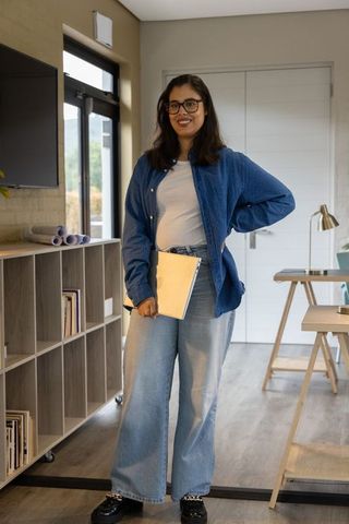 Asian woman standing in modern studio office holding beige folder, casual professional