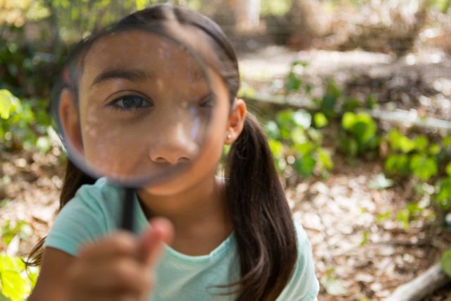 This close-up image of a little girl holding and looking through a magnifying glass in a forest can be used for educational and nature themes. It is perfect for promoting children's activities, curiosity, and learning about the environment. Great for use in blogs, educational materials, and advertisements related to outdoor play and discovery.