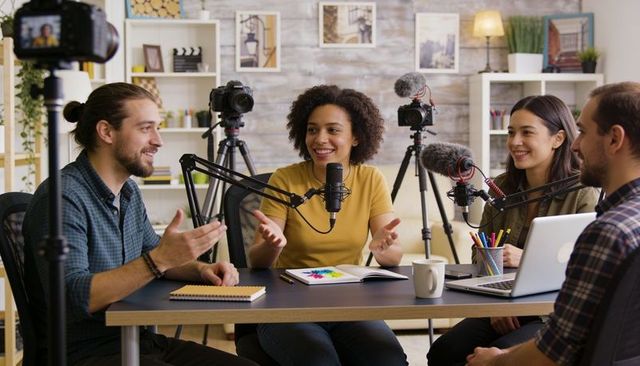 Diverse team recording lively podcast in home studio with microphones, cameras and laptop