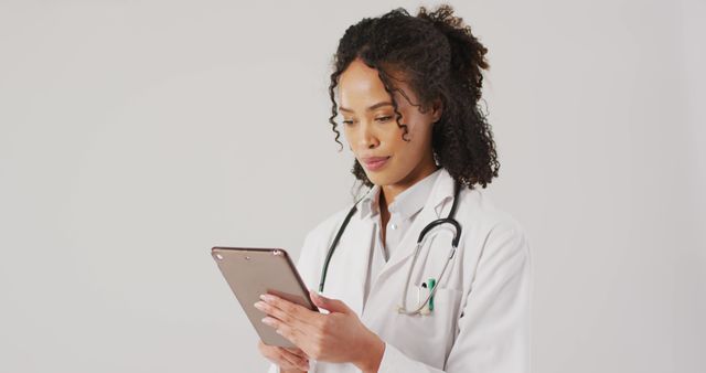 African-American female doctor confidently interacting with a tablet, showcasing modern medical practice. The doctor is in a medical uniform with a stethoscope around her neck, representing professionalism and competence. This can be used for healthcare advertisements, medical blog headers, or presentations on digital health solutions.