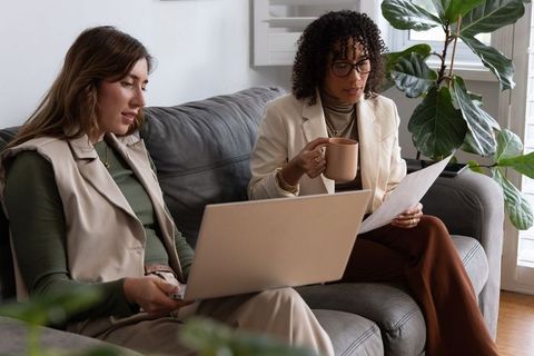 Two diverse female colleagues collaborating on laptop and documents in casual home office