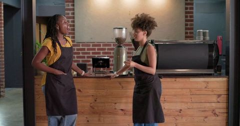 Baristas chatting behind wood counter in cozy brick coffee shop with espresso machine