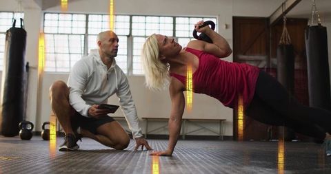 Female athlete performing kettlebell side plank while coach monitoring technique on tablet