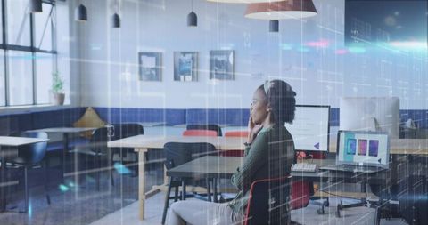 Woman in open-plan office analyzing data on computer monitor