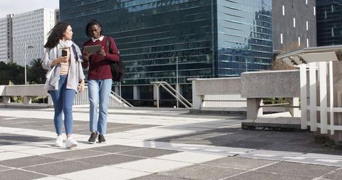 Colleagues walking and collaborating using tablet and smartphone on modern urban plaza