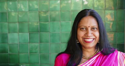 Smiling indian woman in vibrant pink sari against green tiled wall