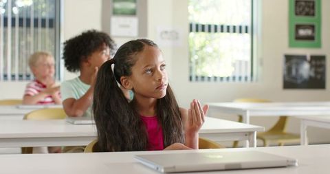 African American Girl Raising Hand in Contemporary Classroom with Laptop and Notebooks