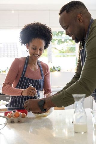 African american couple cooking together in bright modern kitchen whisking eggs, smiling