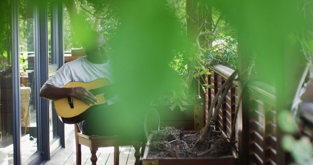 Thoughtful african american senior man sitting on balcony playing acoustic guitar - Download Free Stock Photos Pikwizard.com